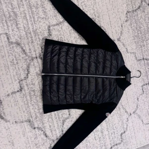 Svart dunjacka från Moncler - Säljer en snygg svart dunjacka från Moncler i mycket bra skick. Jackan har en stilren design med långa ärmar och en praktisk dragkedja framtill. Perfekt för höst och vår när du vill hålla dig varm och trendig. Passar både till vardags och lite finare tillfällen.