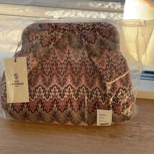 Mönstrad väska från beck söndergaard - Säljer en superfin väska från Beck söndergaard med ett unikt mönster i rosa, brunt och beige. Väskan är helt ny och ouppackade och perfekt för att ge en färgklick till din outfit. Den har en quiltad design som ger en lyxig känsla. Perfekt för både vardag och fest! Det är en kuvertväska🩷