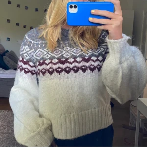 Vit och grå stickad tröja med mönster - LÅNADE BILDER! Superfin stickad tröja i vitt och grått med ett snyggt mönster i vinrött och vitt runt halsen. Den har långa ärmar och en skön, ribbad kant vid ärmslut och nederkant. Perfekt för kyliga höst- och vinterdagar! 