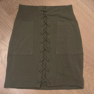 Olivgrön kjol från Guess - Snygg olivgrön kjol från Guess i storlek XS. Kjolen har en cool snörning framtill och praktiska fickor. Perfekt för både vardag och fest! 💚