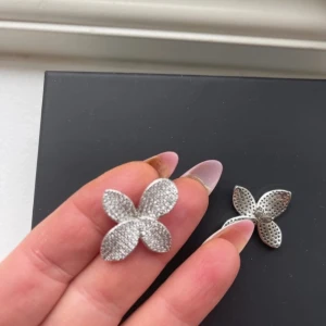 Glittriga blomformade örhängen - Säljer ett par superfina örhängen i form av blommor. De är i silverfärg och täckta med glittriga stenar som verkligen fångar ljuset. Perfekta för att ge lite extra bling till din outfit, oavsett om det är till fest eller vardag. De är i mycket bra skick och redo att bäras av någon som älskar att glittra!
