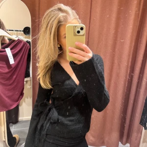 Svart omlott tröja - Säljer en snygg svart omlott tröja med knytning i sidan. Perfekt för höst och vinter, den är både stilren och bekväm. Helt ny, prislappen kvar! SLUTSÅLD