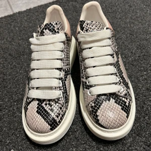 Sneakers med ormskinnsmönster från Alexander McQueen - Säljer ett par snygga sneakers från Alexander McQueen i ormskinnsmönster. Skorna har en chunky vit sula och breda vita snören. De är i mycket bra skick och perfekta för att ge din outfit en edgy touch. Passar både till vardags och fest!