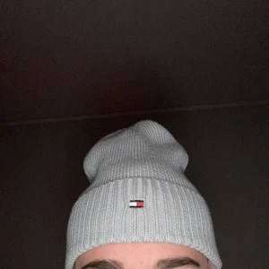 Grå mössa från Tommy Hilfiger - Säljer en snygg grå mössa från Tommy Hilfiger i storlek L/XL. Den är stickad och har en liten broderad logga framtill. Perfekt för att hålla sig varm under höst och vinter. Mössan är i mycket bra skick och passar perfekt nu inför vintern.