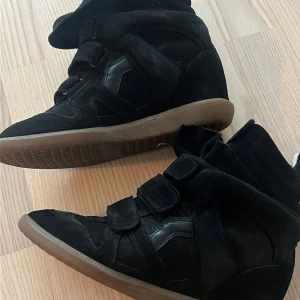 Isabel marant, svarta sneakers med kilklack - Säljer ett par svarta sneakers i mocka med kilklack. De har en cool design med flera kardborreband och en hög ankel. Perfekta för att ge lite extra höjd och stil till vardagslooken. Använda men i bra skick. Pris kan diskuteras vid snabb affär. 