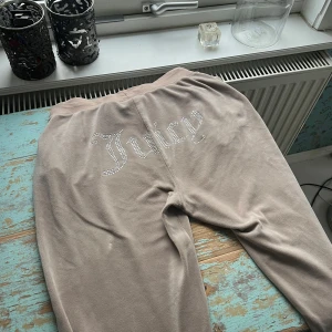 Beige mjukisbyxor från Juicy Couture - Säljer ett par beige mjukisbyxor från Juicy Couture med glittrig text på baksidan. Byxorna är supermjuka och perfekta för en chill dag hemma. Det finns ett litet hål på ena benet, men annars i bra skick. Perfekt för höstmys! 🍂