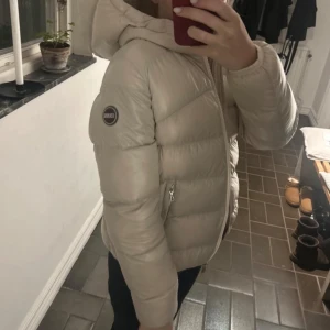 Beige dunjacka från Colmar - Säljer en snygg beige dunjacka från Colmar i mycket bra skick. Jackan har en mysig huva och praktiska dragkedjor på fickorna. Perfekt för kalla vinterdagar! Den är långärmad och har en normal passform. Supervarm och stilren, perfekt för både vardag och utflykter.