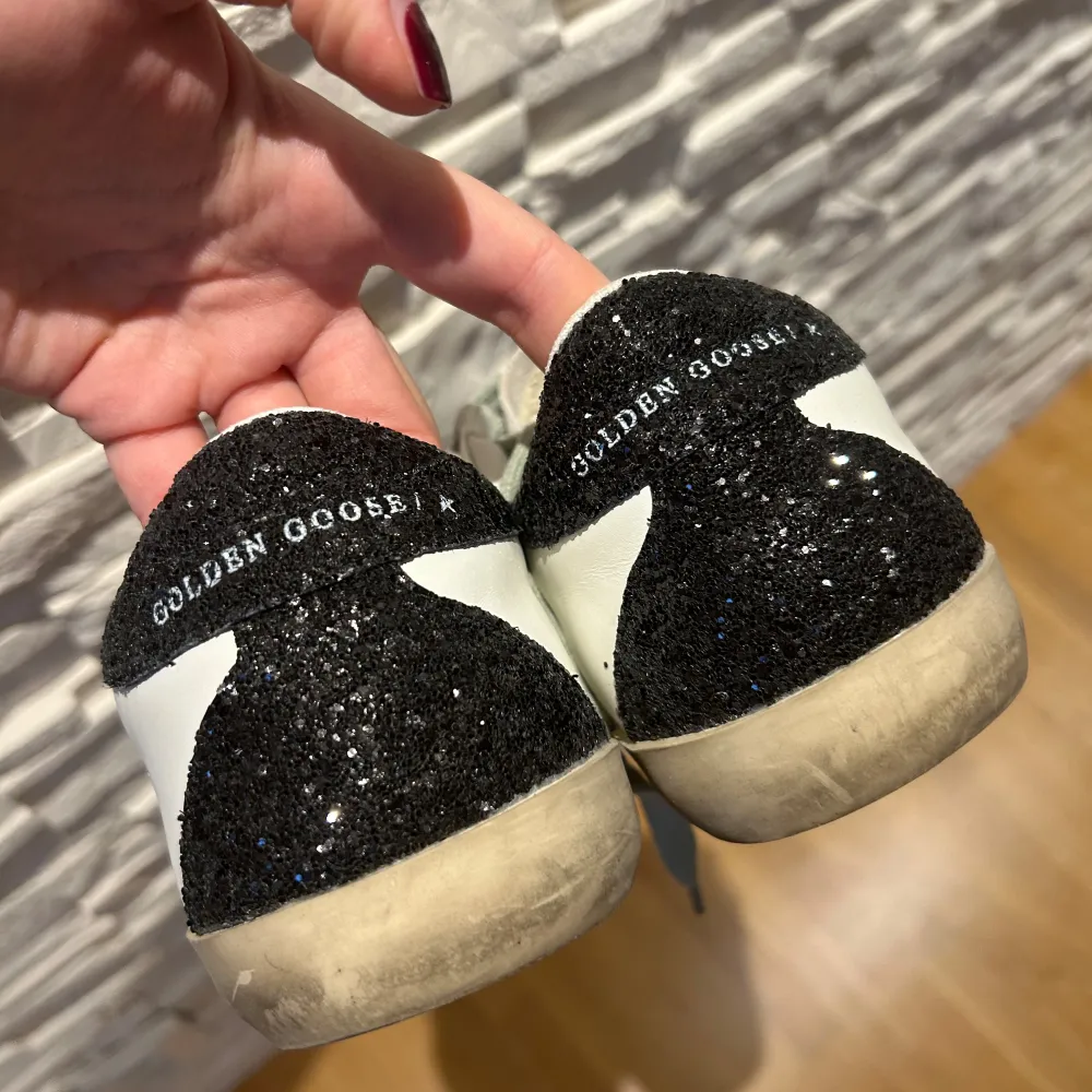 Säljer ett par snygga Golden Goose sneakers i vitt skinn med en glittrig silverstjärna på sidan. Skorna har grå snörning och svart glittrig häl. Perfekta för att ge din outfit lite extra bling! . Skor.