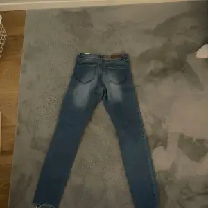 Säljer ett par snygga blå skinny jeans med slitningar på framsidan. De har en klassisk femficksdesign och är perfekta för en avslappnad stil. Jeansen är i bra skick och passar perfekt till vardags. Dem är lätta att sy om till boot cut 