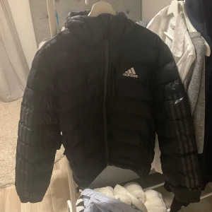 Svart dunjacka från Adidas - Säljer en svart dunjacka från Adidas i mycket bra skick. Perfekt för kalla höst- och vinterdagar. Jackan är mycket sparsamt använd under en vinter. Storlek M, men skulle säga att den är som en S/M!