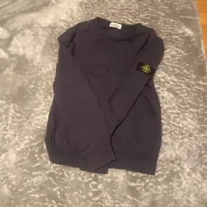 Säljer en snygg mörkblå tröja från Stone Island. Den har en klassisk design med långärmad stil och det ikoniska märket på ärmen. Perfekt för både vardag och lite mer avslappnade tillfällen. Tröjan är i bra skick och redo för en ny ägare! Inga skador! 