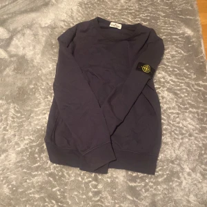 Mörkblå/ lila tröja från Stone Island - Säljer en snygg mörkblå tröja från Stone Island. Den har en klassisk design med långärmad stil och det ikoniska märket på ärmen. Perfekt för både vardag och lite mer avslappnade tillfällen. Tröjan är i bra skick och redo för en ny ägare! Inga skador! 