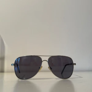 Svarta pilotglasögon från Prestige - Snygga svarta pilotglasögon från Prestige med en klassisk design. De har en tunn metallram och mörka glas som ger ett stilrent intryck. Perfekta för soliga dagar och ger en cool look.