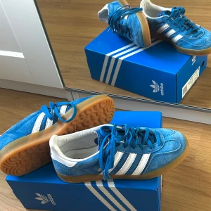 Blå Adidas Gazelle  - Snygga fåtal använda blå Adidas Gazelle Indoor sneaker. Skorna har en klassisk design med snörning och är perfekta för en sportig look. Går även ihop med olika typer av outfit och passar nästan som storlek 38 också. Inkluderar extra vita skosnöre:) 