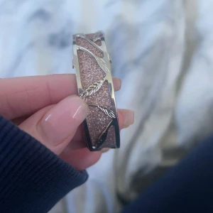 Silvrigt armband från les georgettes - Snyggt armband med glittrig yta i rosa och eleganta silverdetaljer i form av blad. Perfekt för att ge en extra touch till din outfit. från les georgettes, nypris 650kr då det bara fanns ett visst antal av just denna. det rosa bandet kan man byta till andra färger då det går att köpa till nya ”band”💕armbandet är töjbart och passar därför alla💗
