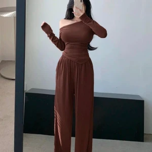 Brun byxdress med off-shoulder design - Snygg brun byxdress med off-shoulder design och långa ärmar. Byxdressen har en åtsittande överdel och vida byxben, vilket ger en elegant och bekväm look. Perfekt för en stilren outfit.