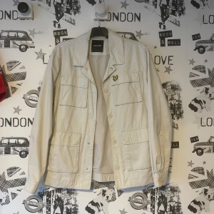 Beige jacka från Lyle & Scott - Säljer en stilren beige jacka från Lyle & Scott. Jackan har långa ärmar och flera praktiska fickor framtill. Perfekt för en avslappnad look. Använd 1 gång