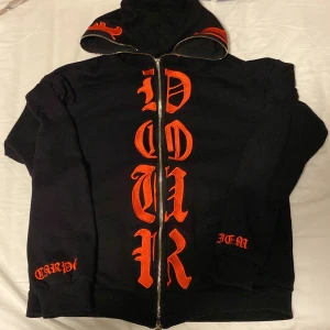 Svart hoodie med röd text - Säljer en svart hoodie med röd text. Den har en dragkedja framtill och texten 'CARPE DIEM' på ärmen och nedtill. Perfekt för en cool och avslappnad stil.