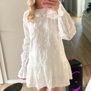 Vit blommig klänning - Charmig vit klänning med blommigt mönster och långa ärmar. Klänningen har en lös passform och knytning i ryggen. Perfekt för sommaren eller studenten!! Köpt för ungefär 700, mitt pris 400 då den endast är använd en gång!