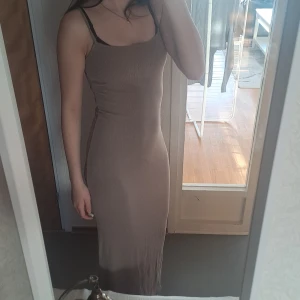 Beige långklänning med smala axelband - Snygg beige/ olivgrön   långklänning med smala axelband. Klänningen har en tight passform och är perfekt för en stilren look. Den är tillverkad i ett mjukt och bekvämt material som formar sig fint efter kroppen.