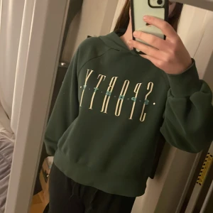 Grön hoodie med tryck  - Säljer en grön hoodie med texten 'SPORTY' i en stilren design. Tröjan har en bekväm passform med långa ärmar och en klassisk huva. Perfekt för en avslappnad stil. Tröjan är superfin men kommer tyvärr inte till användning längre💚✨✨