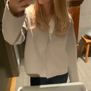 Beige kappa - Säljer en stilren beige kappa  från kapphal Den har en enkel design med v-ringning och långa ärmar. Perfekt för en minimalistisk look. Passar bra till både jeans och kjol.