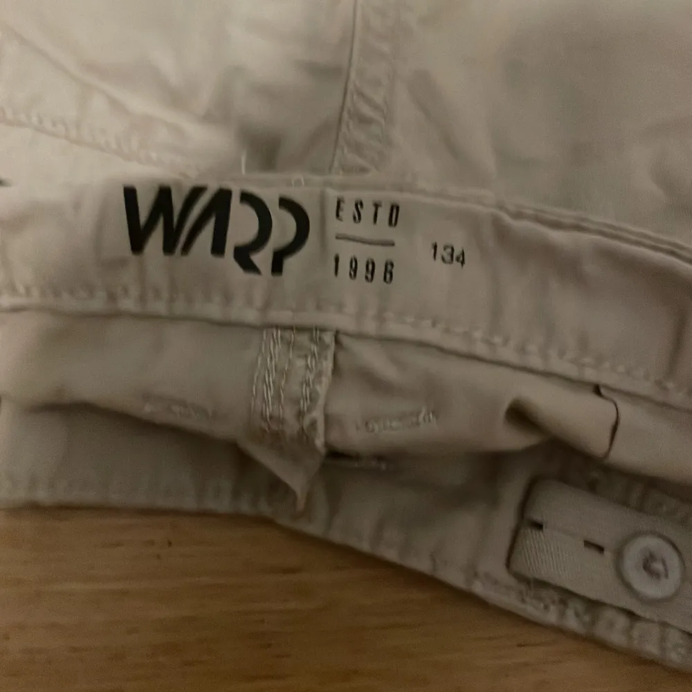 Säljer ett par beige shorts från Warp. De har en dragkedja och knapp framtill samt en praktisk ficka med dragkedja på sidan. Perfekta för en avslappnad stil.. Shortsit.
