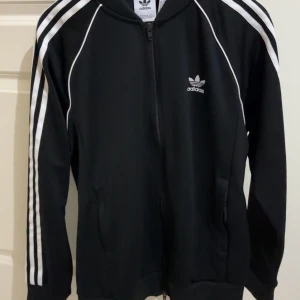 Adidas zip tröja - Klassisk svartvit adidas original zip tröja i polyester. Inte använd så många gånger. Storleken är Large