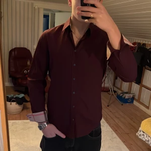 Vinröd skjorta från Burberry Brit - Snygg vinröd skjorta från Burberry med klassiskt rutigt mönster på insidan av kragen och ärmsluten. Storleken är medium och jag som är på bilden är 184 cm lång. Tycker ni inte priset är bra så skriv till mig så löser vi nåt där båda blir nöjda.  Har ni några frågor eller funderingar är det bara att höra av sig