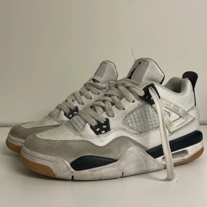 Jordan 4 i vitt och svart från Nike  - Snygga Nike Air Jordan 4 i vitt med svarta detaljer. Skorna har snörning och en klassisk design med Nike SB-logga på hälen.