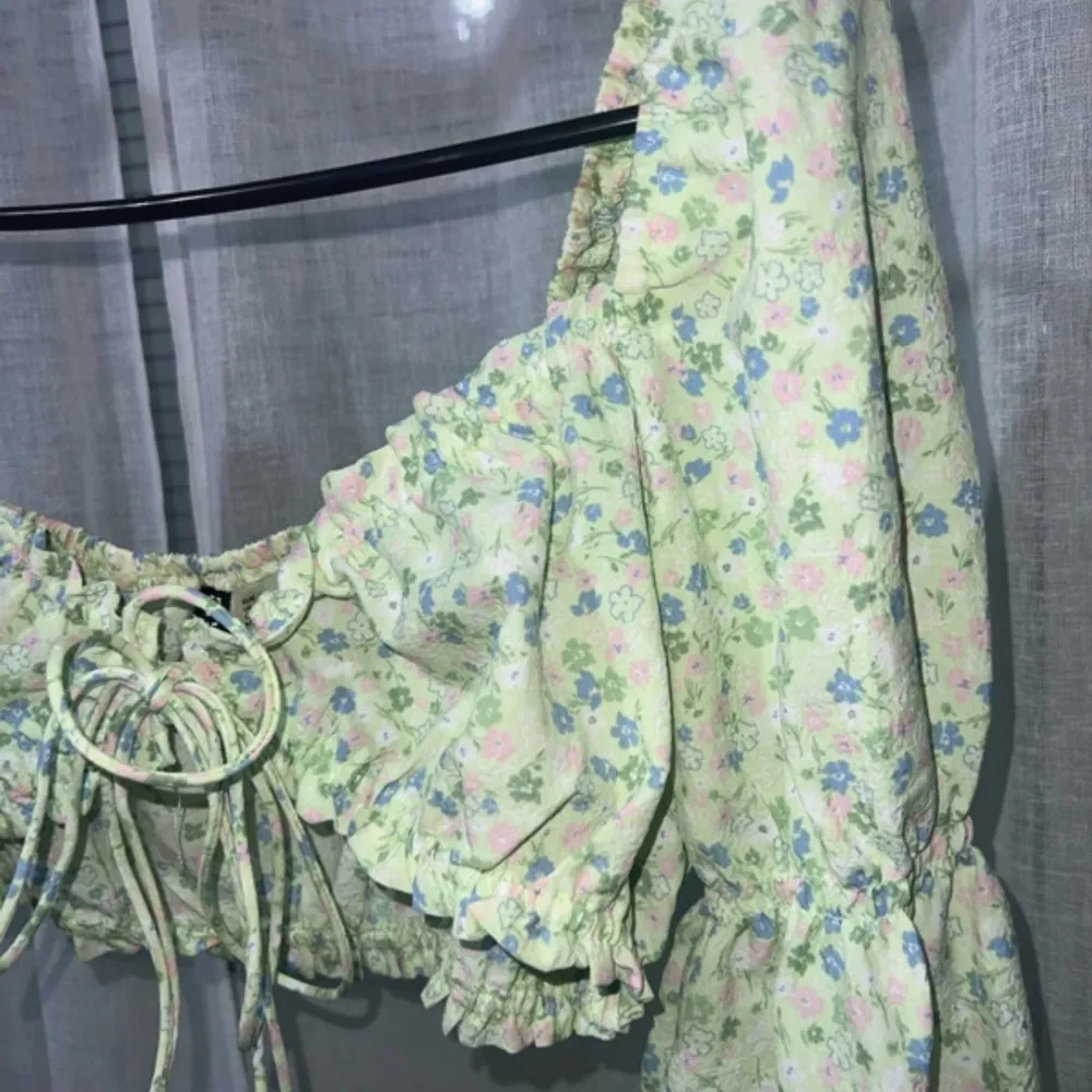 Söt blommig topp i ljusgrönt med små blommor i rosa och blått. Toppen är croppad med volangdetaljer och har långa ärmar. . Yläosat.