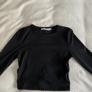 Svart ribbad topp från NA-KD - Svart långärmad topp från NA-KD med öppen rygg och knytning. Använd ett fåtal gånger.