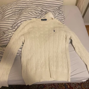 Vit stickad tröja från Ralph Lauren - Säljer en klassisk vit stickad tröja från Ralph Lauren med kabelstickat mönster. Tröjan har långa ärmar och en broderad logotyp på bröstet. Perfekt för en stilren look. Det står medium men det är en small skulle jag säga skriv vid funderingar 