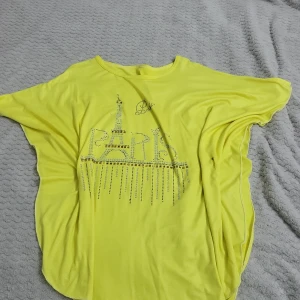 Gul t-shirt med Paris-tryck - Säljer en gul t-shirt med ett glittrigt Paris-tryck på framsidan. T-shirten har korta ärmar och en lös passform, perfekt för en avslappnad stil.