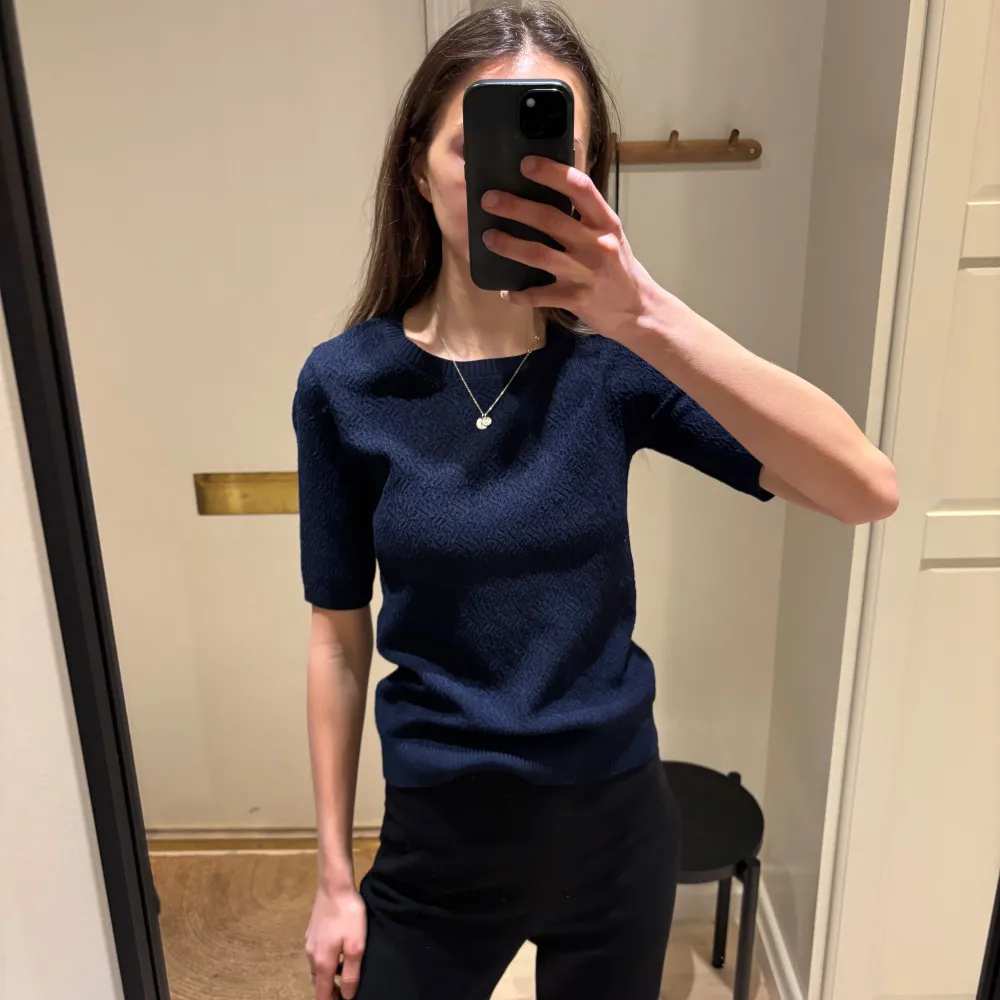 Snygg mörkblå tröja från Stockhlm med korta ärmar och ett diskret mönster. Perfekt för en stilren look. . Neuletakit & Villapaidat.