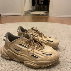 Beige sneakers från Adidas Originals - Säljer ett par snygga beige sneakers från Adidas med en futuristisk design. Skorna har snörning och märkets logotyp på sidan. De har en robust sula och är perfekta för en trendig look. Storlek 36 2/3