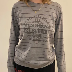 Grunge Grå randig tröja med Times Square-tryck - Säljer en grå randig tröja från EDC med ett coolt Times Square-tryck på framsidan. Tröjan har långa ärmar och en rund halsringning. Perfekt för en avslappnad stil.