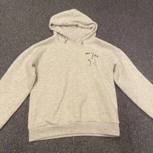 Grå hoodie från Gina Tricot - Säljer en mysig grå hoodie från Gina Tricot med en liten stjärndetalj och text på bröstet. Perfekt för en avslappnad stil. Hoodien har en klassisk design med huva och ribbade muddar vid ärmslut och nederkant.