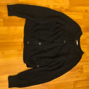 Stickad kofta från Holly & Whyte - Säljer en snygg svart stickad kofta från Holly & Whyte. Koftan har ett fint hålmönster och knappar framtill. Storlek L men funkar bra på mig som egentligen har S. Inga skavanker.