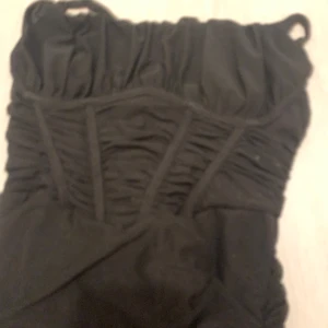 Svart långklänning med rynkade detaljer - Snygg svart långklänning med rynkade detaljer som ger en elegant look. Klänningen har smala axelband och en figurnära passform som framhäver silhuetten. Perfekt för en kväll ute eller en speciell tillställning.