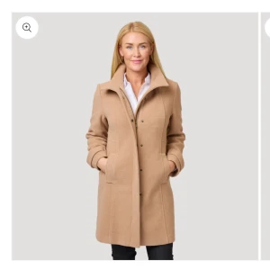 Beige kappa  - Helt ny. Beige klassisk kappa med skorstenskrage i blandmaterial med ull. Snygg helfodrad kappa med tvåvägs dragkedja och tryckknappar framtill. Jackan är avtagen i midjan och har formade sömmar för en smickrande passform. Nypris 1998kr.