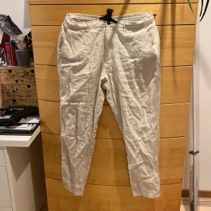 Beige linnebyxor från Zara - Säljer ett par stilrena beige linnebyxor från Zara. Byxorna har en avslappnad passform med midwaist och dragkedja. Perfekta för en bekväm och luftig stil. Storlek L 32