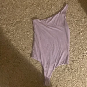 Ljuslila body från BikBok - Snygg ljuslila body från BikBok med en trendig asymmetrisk design och en axel. Perfekt för alla underdelar och årstider . Den har en stilren och modern look som verkligen sticker ut.