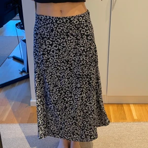 Svart och vit leopardmönstrad kjol - Svart och vit leopardmönstrad kjol med slits framtill. Kjolen har en normal passform, lite utsväng nertill och går till vaderna på mig (jag är 168 cm). Köpt på secondhand, har inga lappar osv så vet ej märke. 