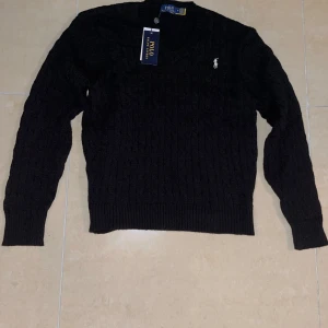 Svart stickad tröja från Polo Ralph Lauren - Säljer en stilren svart stickad tröja från Polo Ralph Lauren. Tröjan har en klassisk design med v-ringning och det ikoniska logotypbroderiet på bröstet. Perfekt för kyligare dagar med sin mjuka och bekväma passform.