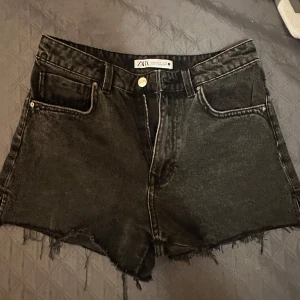 Svarta jeansshorts från Zara - Snygga svarta jeansshorts från Zara med fransiga kanter och klassisk femficksdesign. Perfekta för en avslappnad stil. De har en knapp och dragkedja framtill.