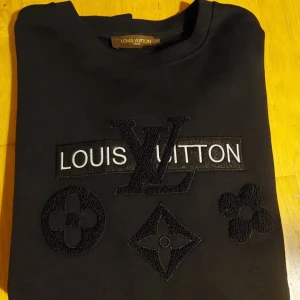 Svart tröja från Louis Vuitton - Snygg svart tröja från Louis Vuitton med broderad logotyp och ikoniska mönster på framsidan. Perfekt för en stilren look. Äkta.
