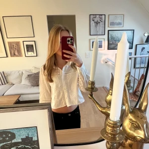 Vit blus med broderade detaljer - Säljer en söt vit blus med broderade detaljer och långa ärmar. Blusen har en fin krage och är croppad, vilket ger en trendig look. Perfekt för att lyfta vilken outfit som helst!