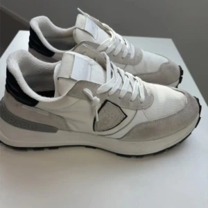 Vita och grå sneakers från Philippe Model - Ett par feta Philippe Model Trainers som är använd mindre än 1 månad. Fått flera komplimanger. Den passar sätill alla stiliga stilar. Oavsett om du kör på en oversized hoodie eller en clean streetwear-look, de här skorna  lyfter din stil. Grisch? 100%.  Säkra dem innan någon annan gör det! Boxen och Qr kod ingår.