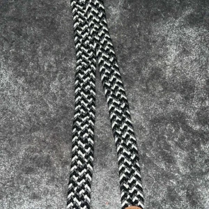 Svartvitt flätat bälte - Snyggt svartvitt flätat bälte med ett coolt mönster. Perfekt för att ge din outfit en extra touch. Passar till många olika stilar och tillfällen. FRÅN ONEWEAR